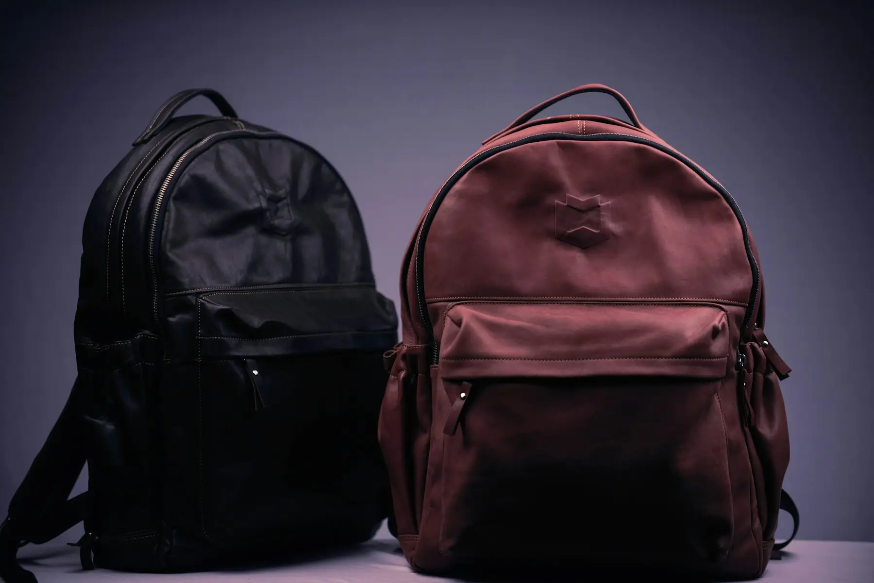 Dos mochilas de piel, una negra y una color vino, lado a lado