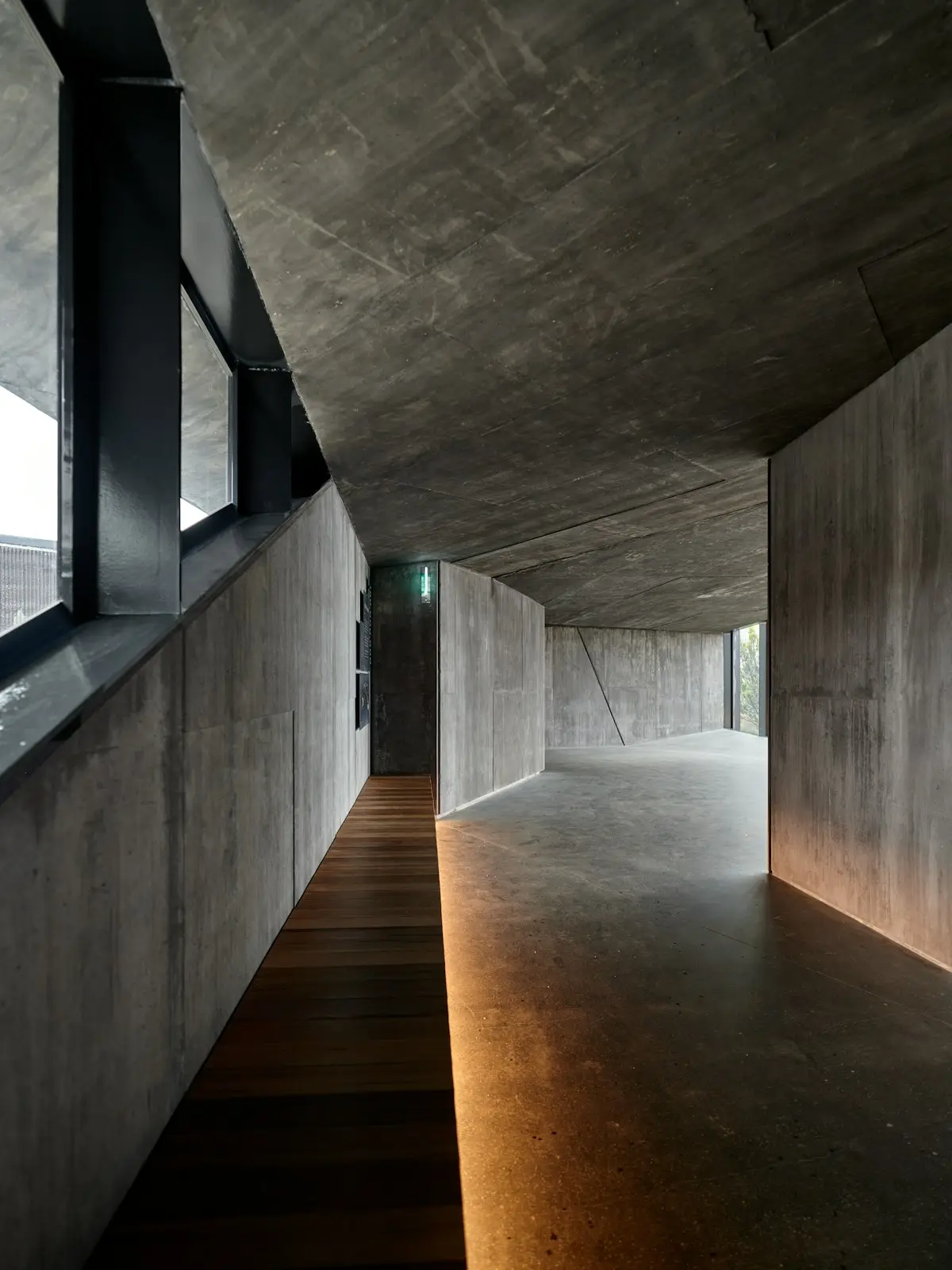 Pasillo de concreto con piso de madera y luz cálida