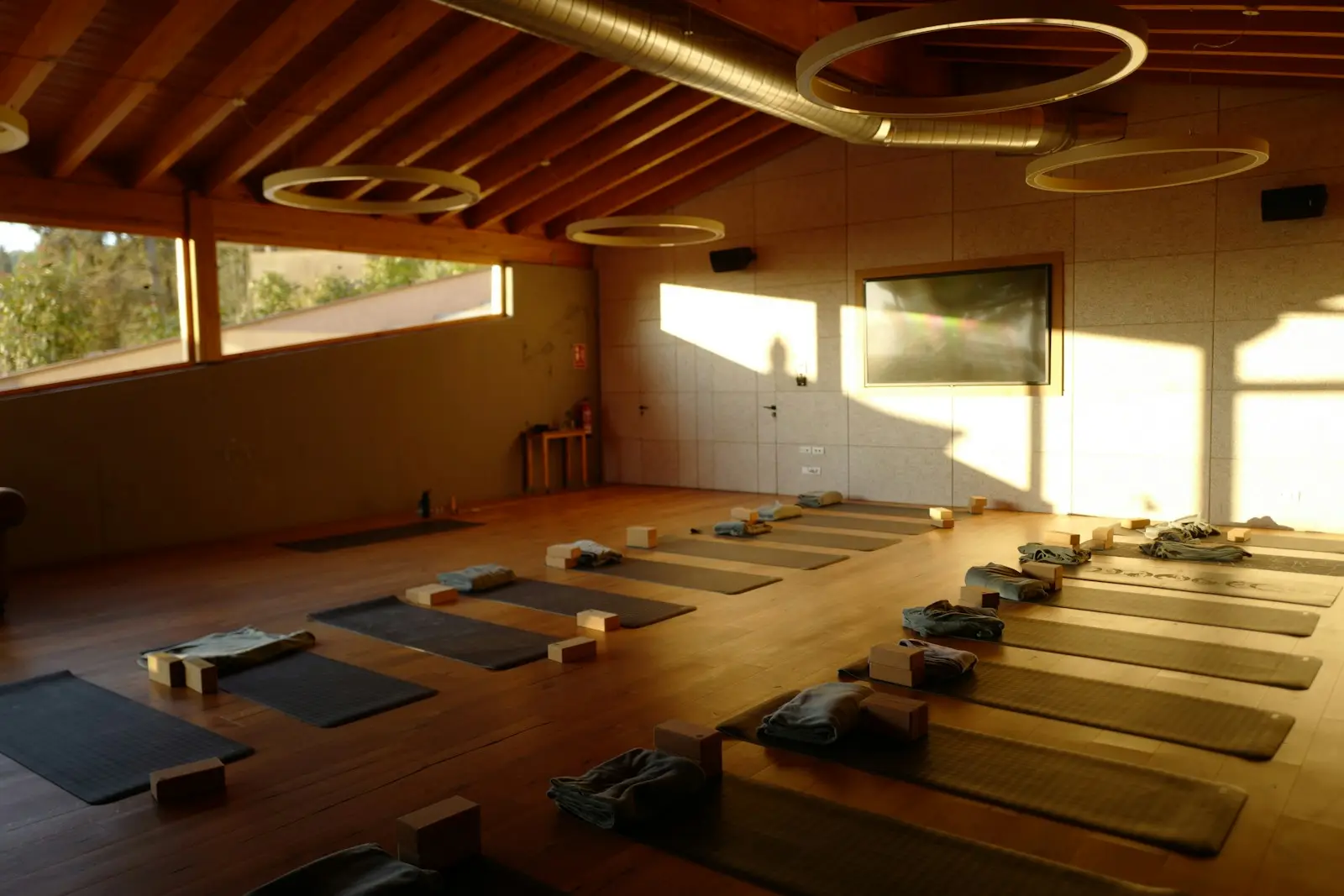Salón de yoga con piso de madera, tapetes alineados y luz de la tarde